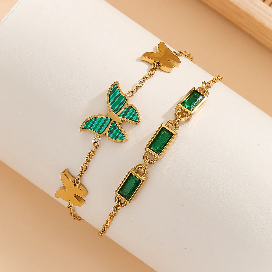 A set of two golden chains with green butterfly and rectangular bead accents.  A golden cuff bracelet with Roman numerals and small crystals.