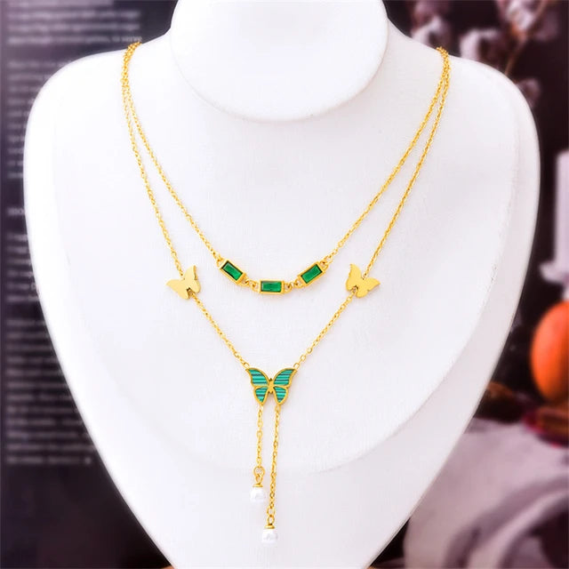 A set of two golden chains with green butterfly and rectangular bead accents.  A golden cuff bracelet with Roman numerals and small crystals.